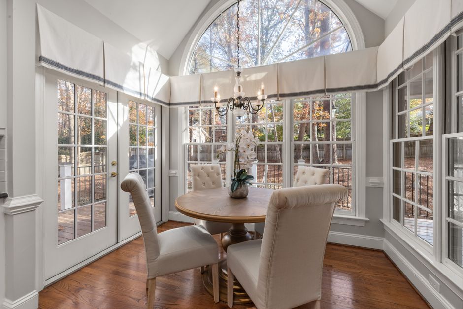 Elegant dining room with a round table, chandelier, and large windows overlooking a garden.