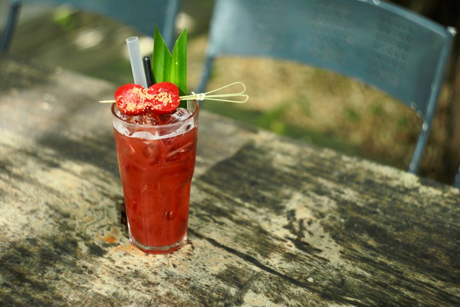 A vibrant iced berry cocktail garnished with fruit and leaves on a weathered wooden table outdoors.