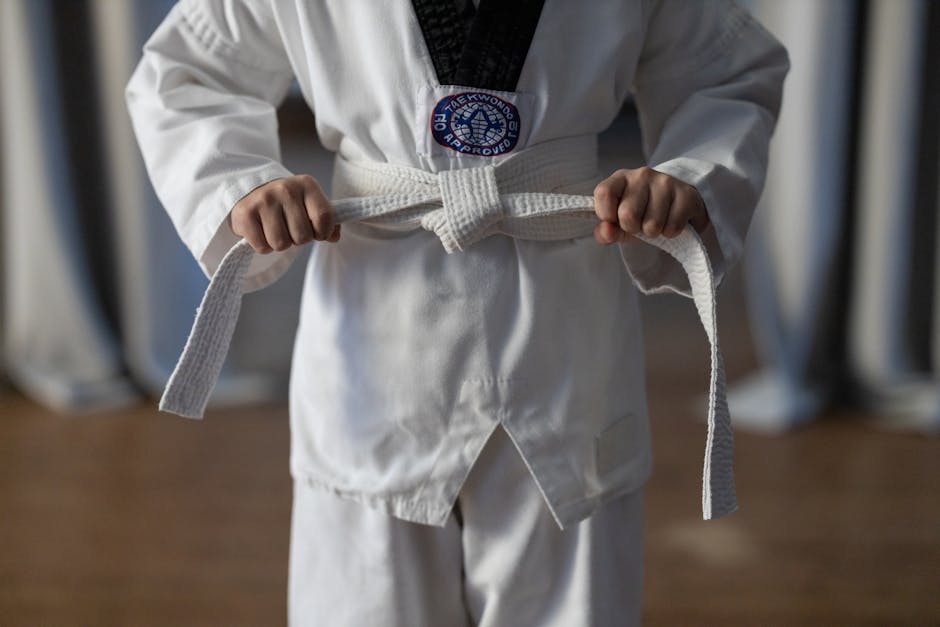 Close-up of a karate student tying a white belt in a traditional martial arts uniform.