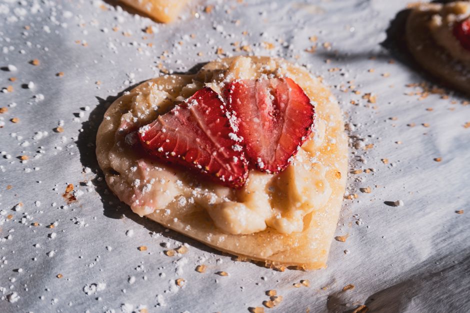 Delicious heart-shaped pastry topped with fresh sliced strawberries and a sprinkle of powdered sugar.