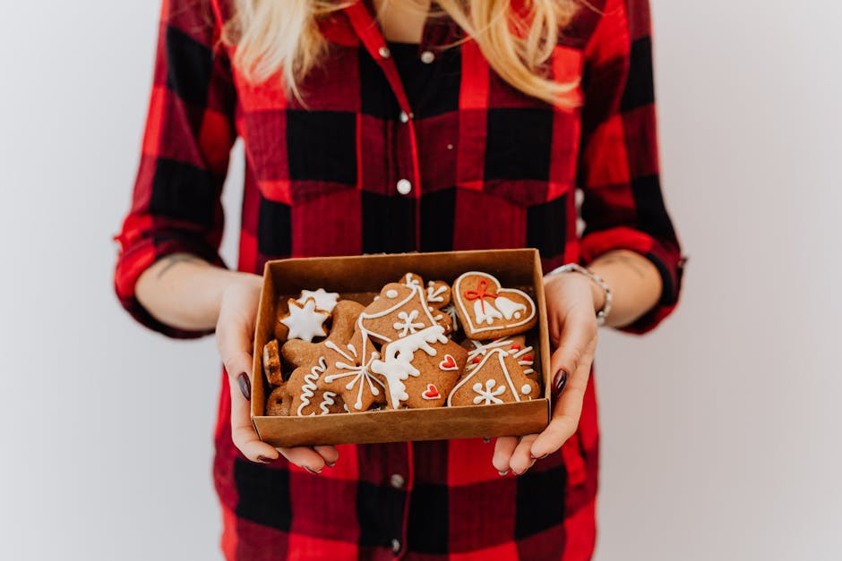 A woman in a plaid shirt holds a festive box of beautifully decorated gingerbread cookies.