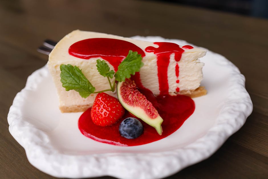 Slice of cheesecake topped with fresh berries, fig, and red sauce on a white plate.