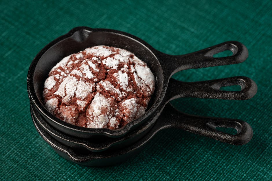 Close-up of a chocolate crinkle cookie in a black mini skillet on a green textured background.