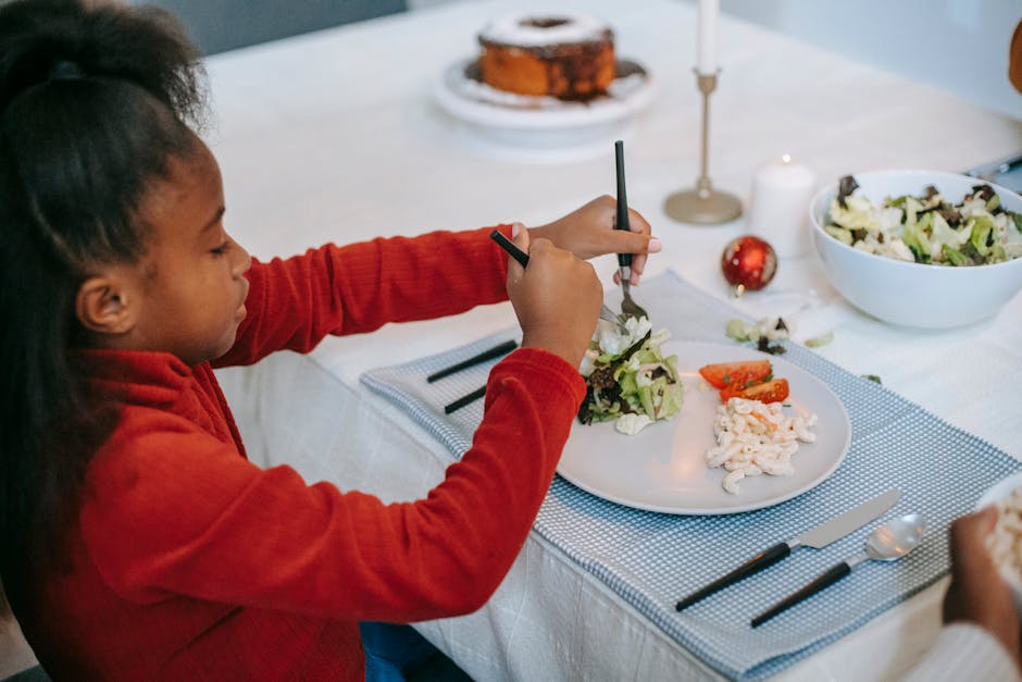 From above side view of African American preteen child putting salad on plate while sitting at table during holiday dinner