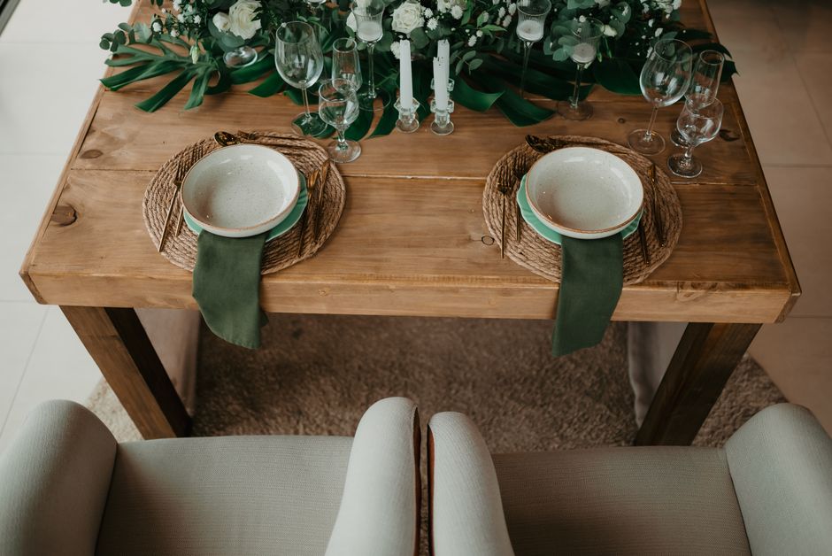 Beautifully arranged rustic dining table with plates, glassware, and green decor indoors.
