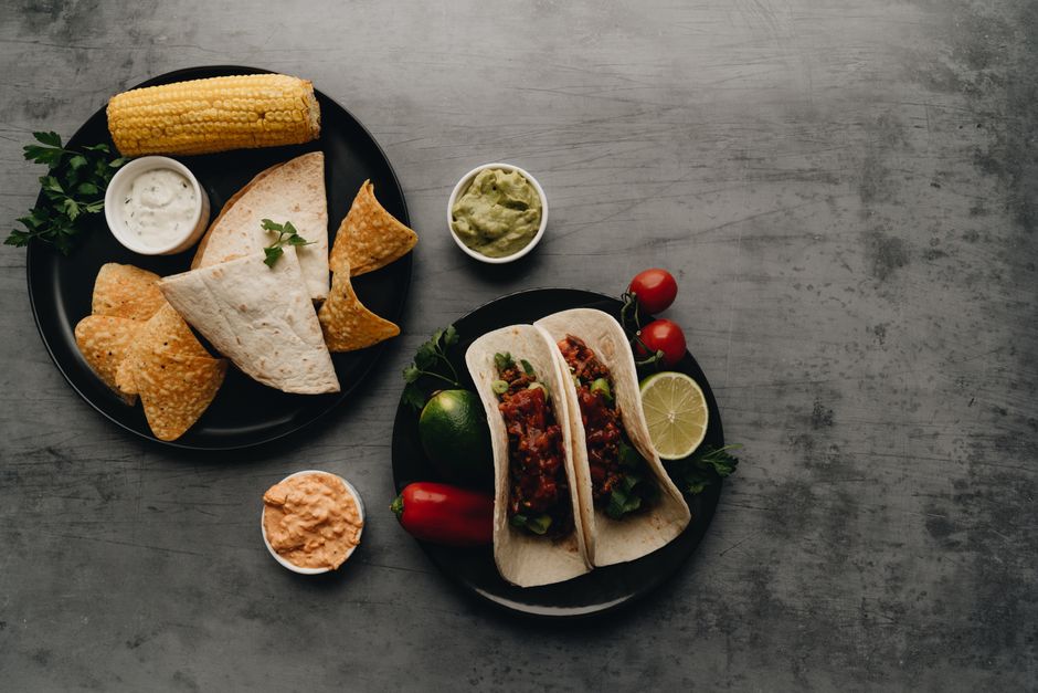 Top view of Mexican cuisine with tacos, chips, and dips on a dark background.
