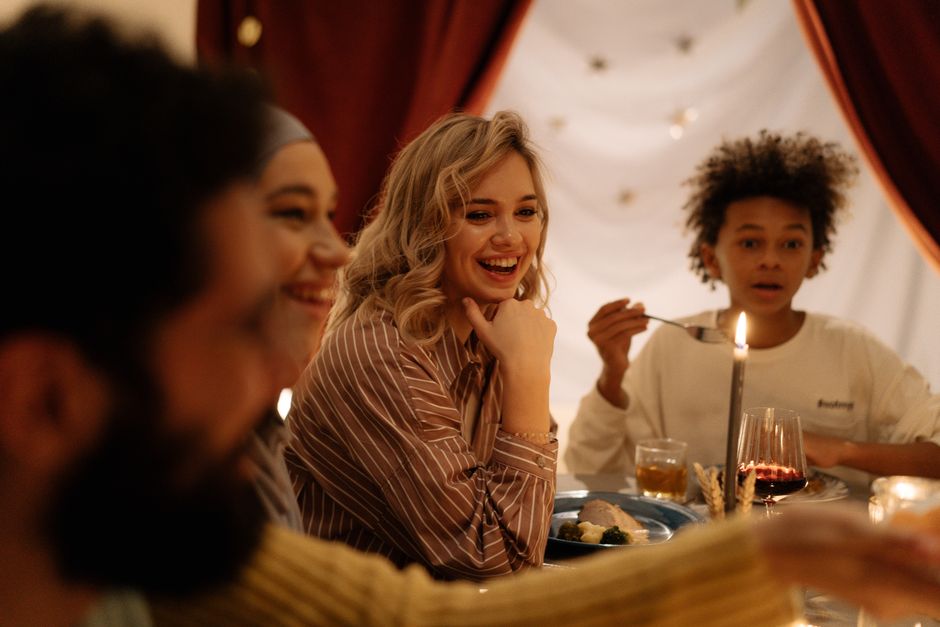 A warm, joyful dinner gathering indoors with diverse friends and family sharing food and laughter.