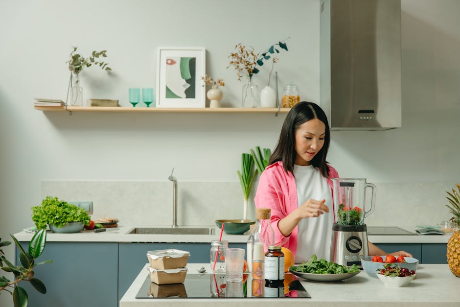 Asian woman blending fresh fruits and vegetables in a stylish kitchen setting.