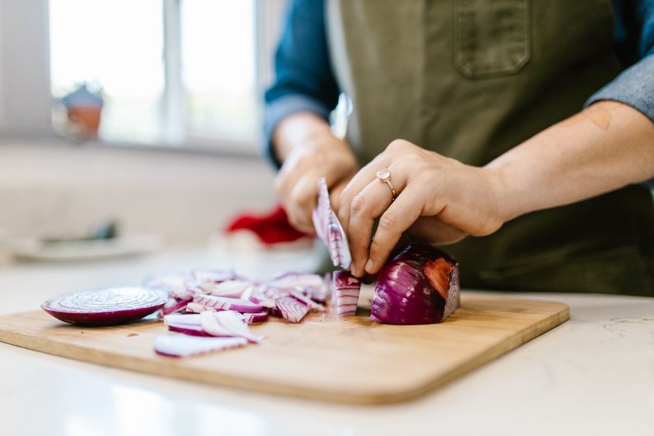 Close-up of a woman chopping fresh red onion in a kitchen setting.