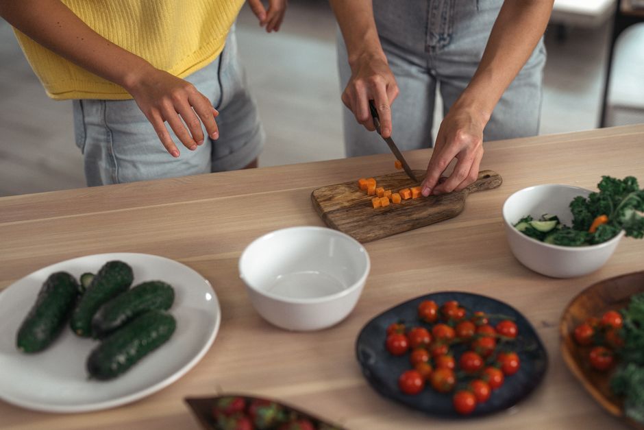 Two people preparing fresh vegetables on a wooden countertop.