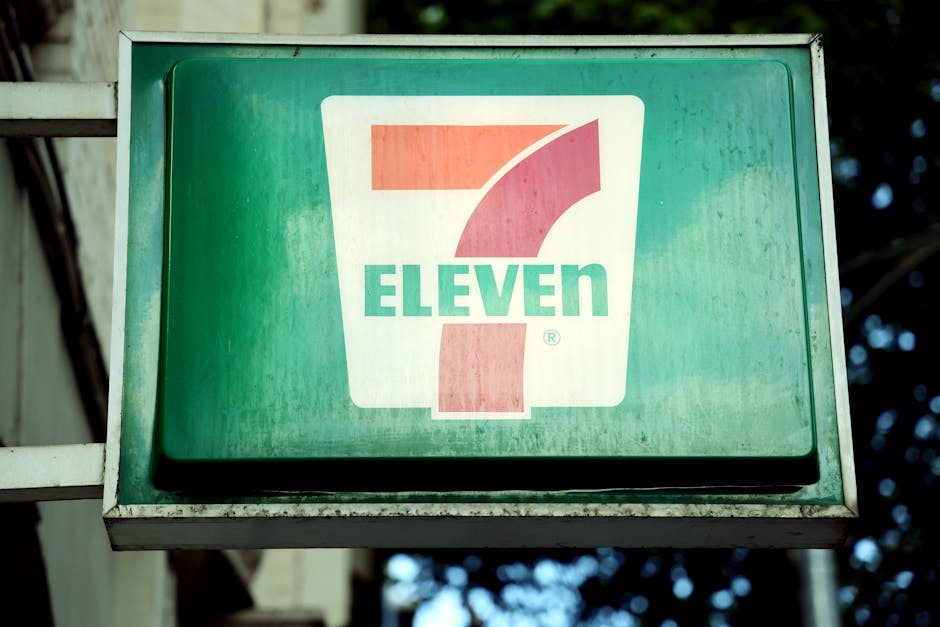 A close-up of a 7-Eleven store sign in a city environment, outdoors.
