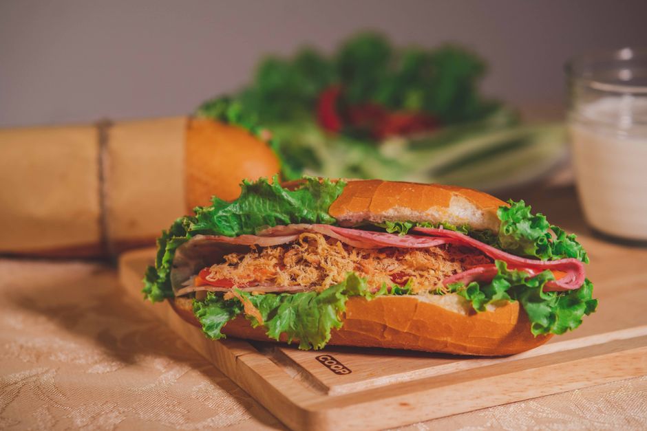 Close-up of a flavorful banh mi sandwich with fresh lettuce, meat, and bread on a cutting board.