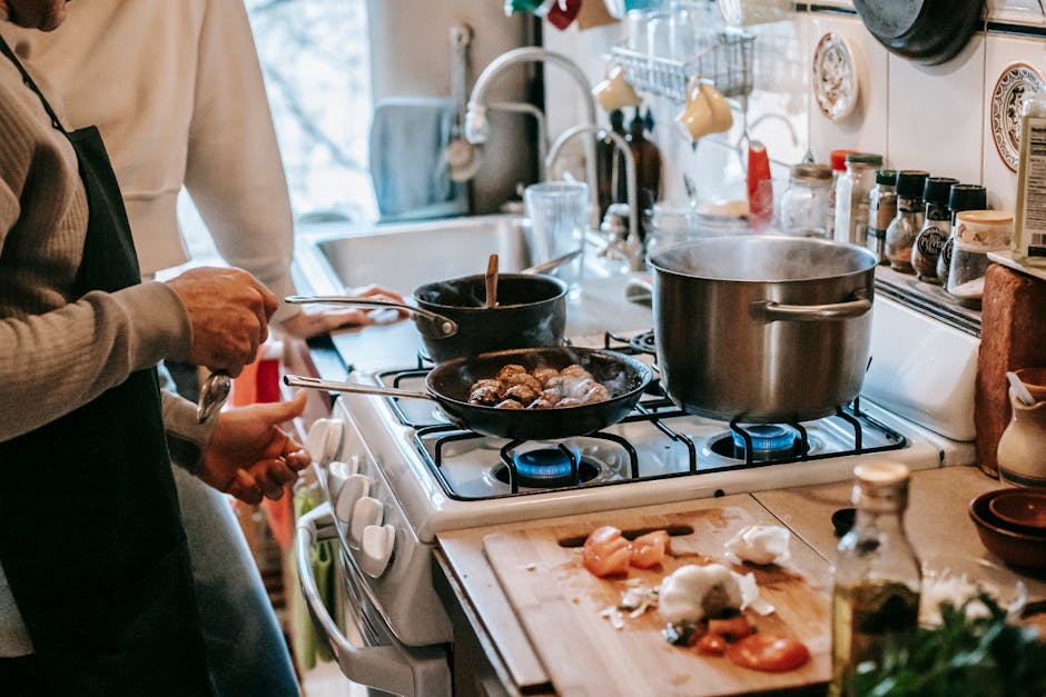 Crop unrecognizable male in casual clothes and apron frying meatballs while preparing delicious dinner standing at stove near wife