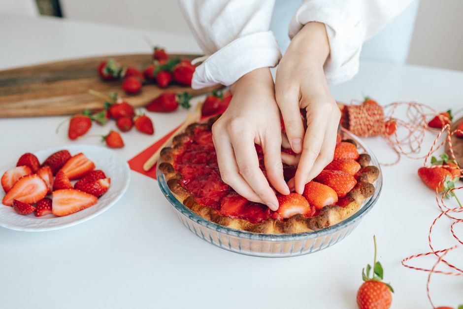 Hands arranging fresh strawberries on a pie, showcasing delicious homemade food preparation.
