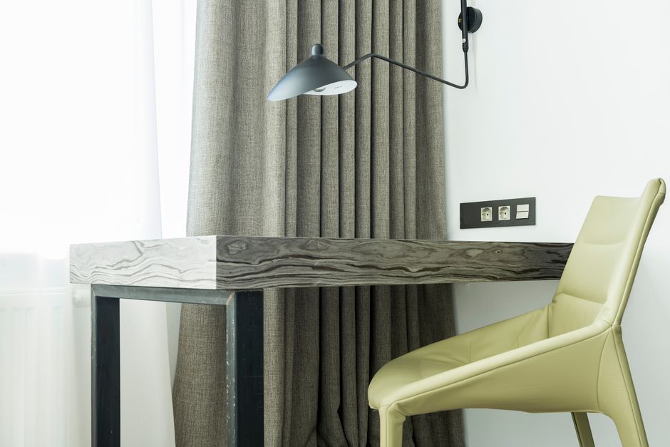 Stylish room with soft leather chair near wooden table and window behind curtain
