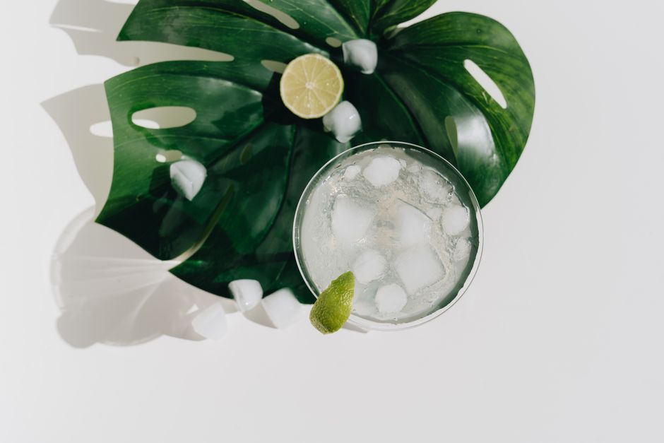 Overhead shot of a margarita with ice on a monstera leaf, garnished with lime. Perfect for a refreshing summer drink.