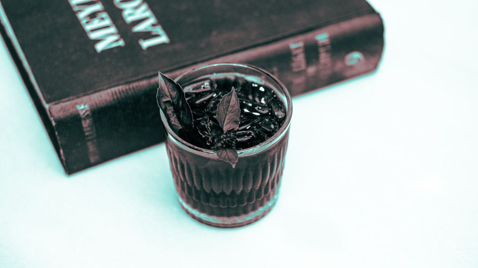 A refreshing cocktail with herbs next to an antique book, perfect for a cozy indoor setting.