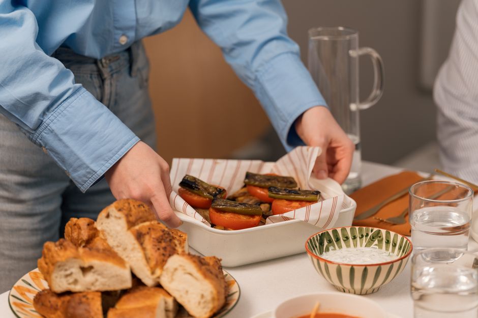A person setting a table with grilled vegetables and bread, perfect for a cozy dinner atmosphere.