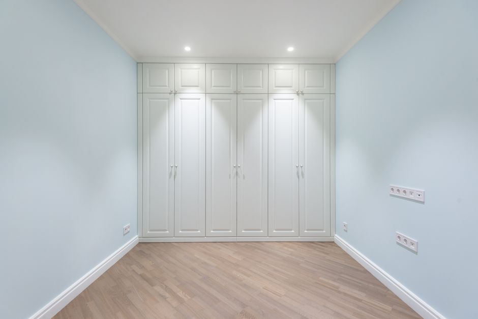 Empty spacious room with parquet floor and built in wardrobe with white doors under glowing lamps
